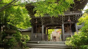 A traditional Japanese temple with a wooden structure, stone steps, and a statue at the entrance.