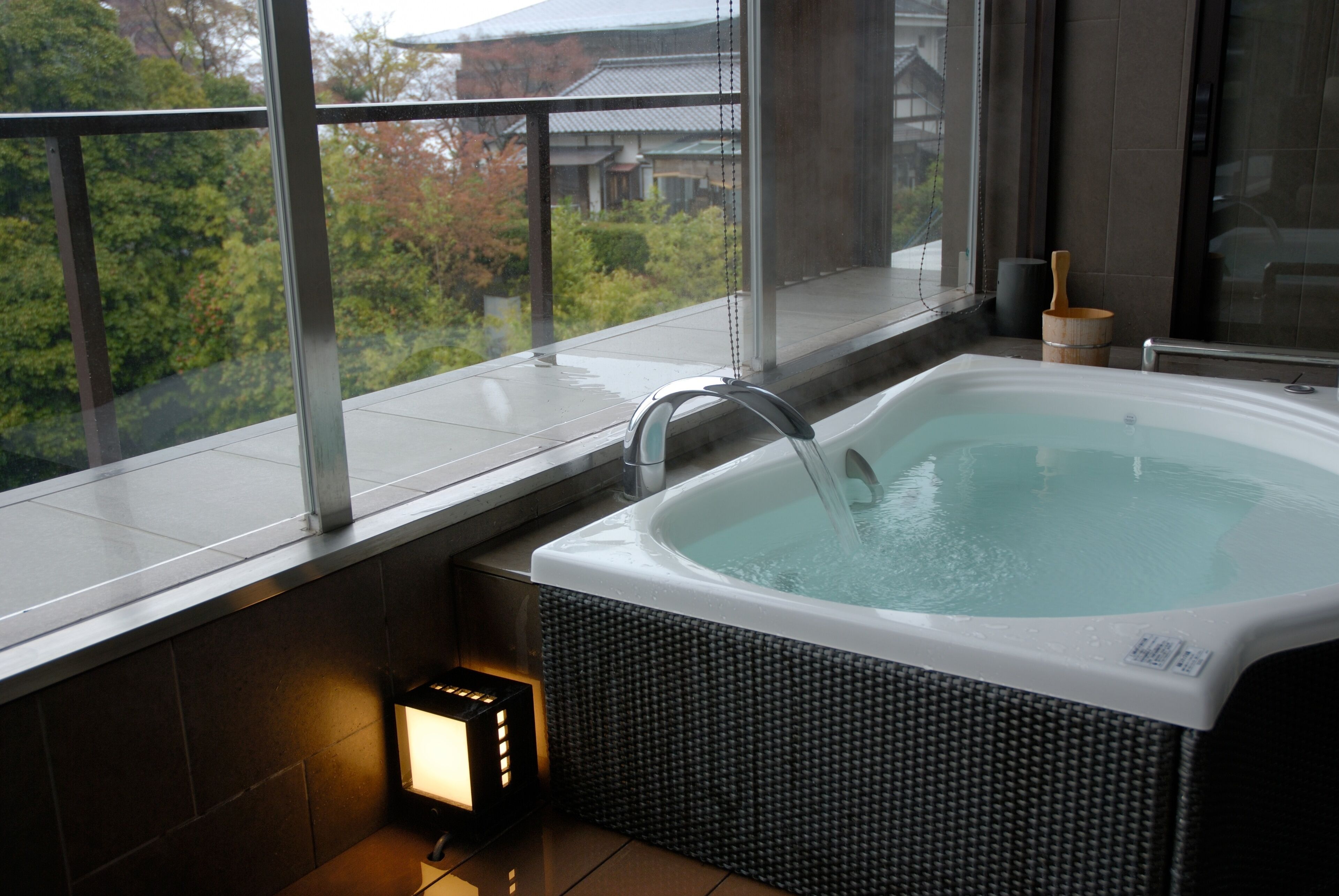 Ett bubbelbad med utsikt över traditionella byggnader och träd genom stora fönster.