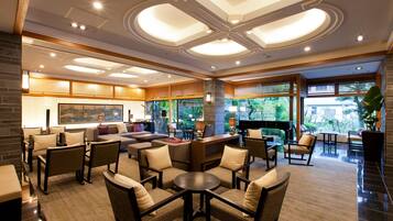 A spacious lobby with a central seating area, a reception desk, and large windows offering a view of greenery outside.