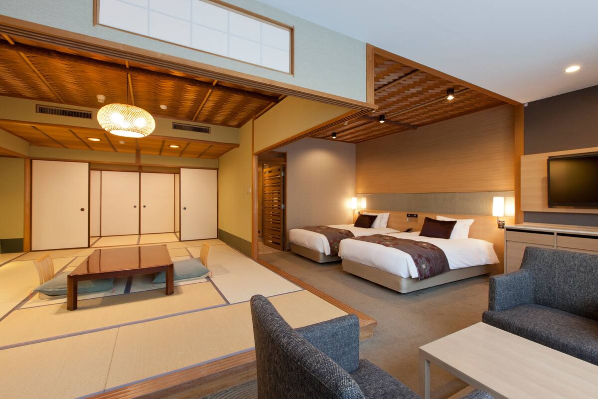 A hotel room with tatami flooring, a sofa, a bed, and a television.