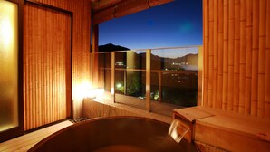 A modern spa room with a large hot tub, wooden walls, and a view of a cityscape at dusk. - Miyajima Grand Hotel Arimoto (Hatsukaichi)