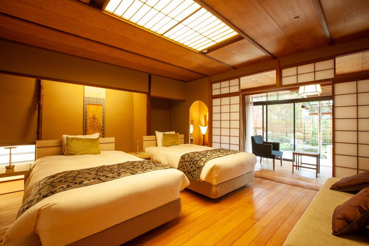 A traditional Japanese-style room with two beds, wooden flooring, tatami mats, and sliding doors leading to a garden.