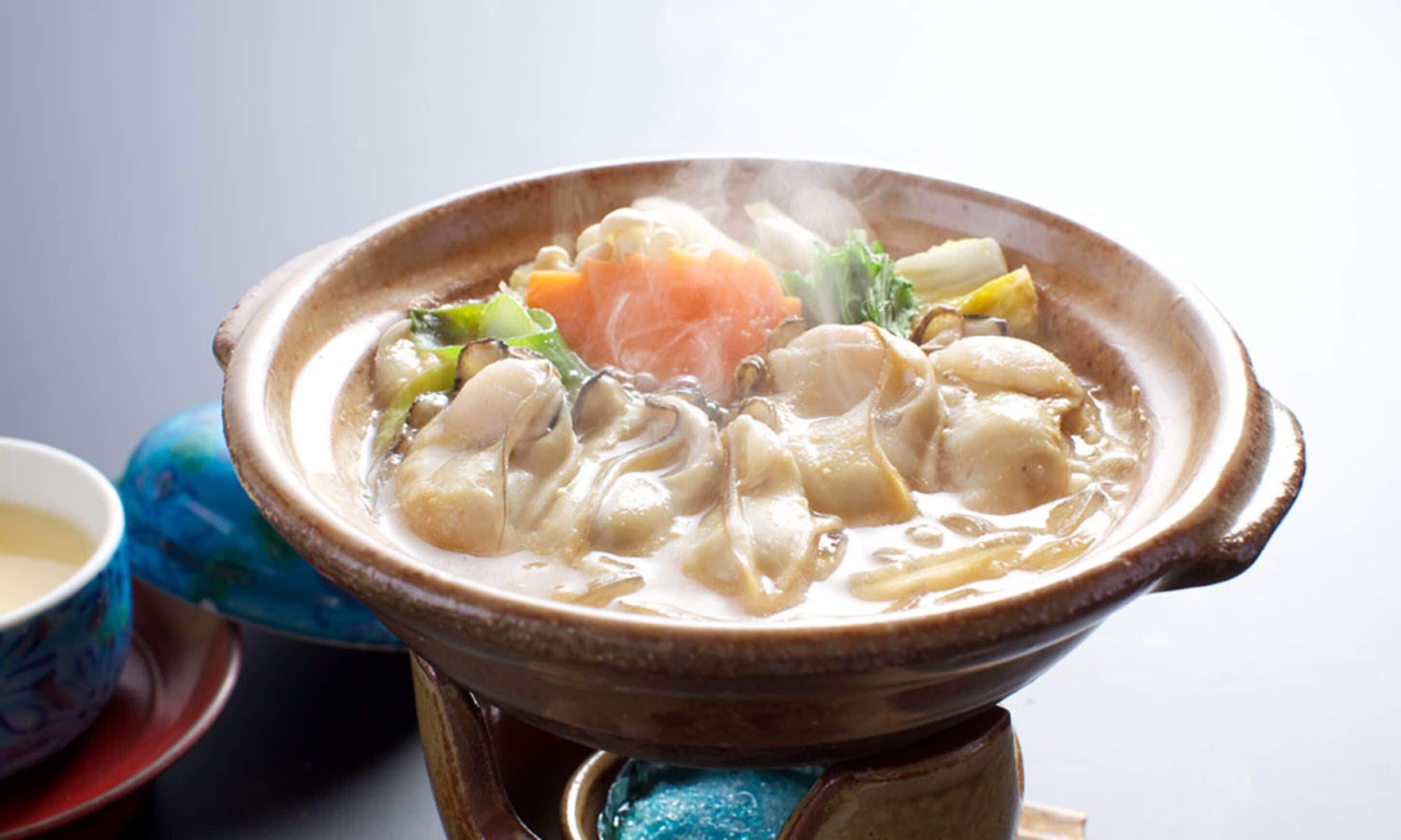 A traditional Japanese hot pot with various ingredients, a ceramic bowl, and a blue patterned cup.