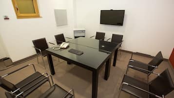 Una sala conferenze con un tavolo in vetro, sedie nere, un telefono e una TV a parete.
