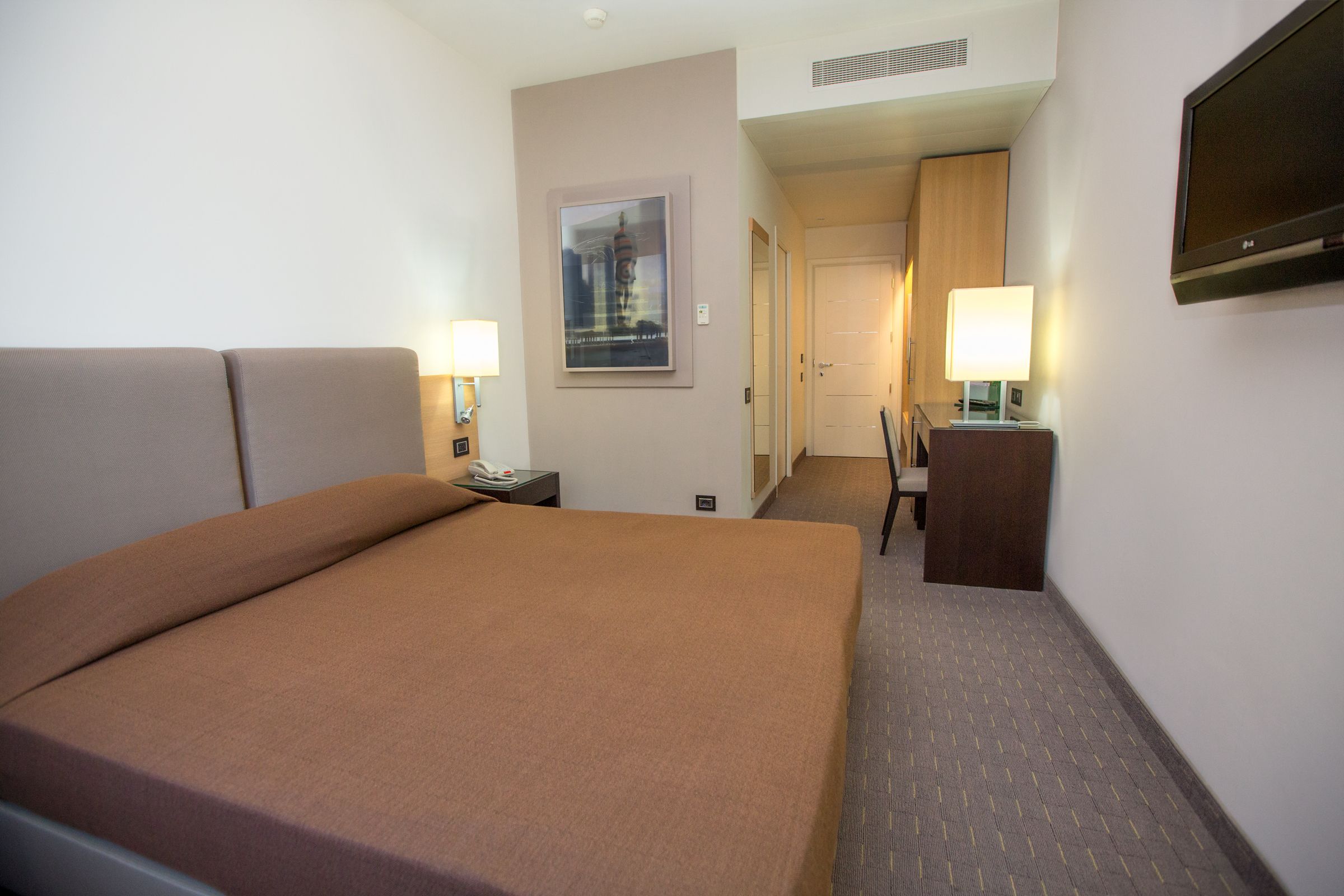 Un cuarto de hotel con una cama grande, dos mesitas de noche con lámparas, un televisor y un cuadro enmarcado en la pared.