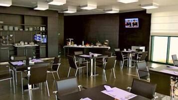 A conference room with tables and chairs, a television screen, and a kitchen area in the background.