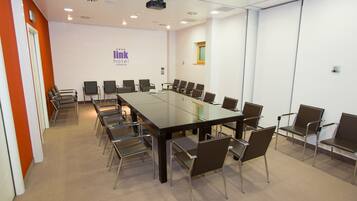 Una sala de conferencias con una larga mesa, sillas y una pantalla para proyector.
