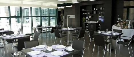 A modern dining area with tables set for meals, large windows, and a black wall with shelves.