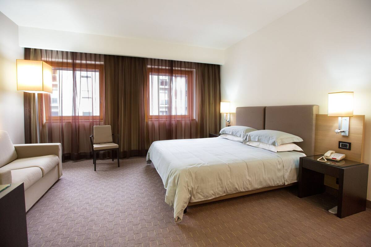 A hotel room with a bed, a chair, a desk, and two lamps.