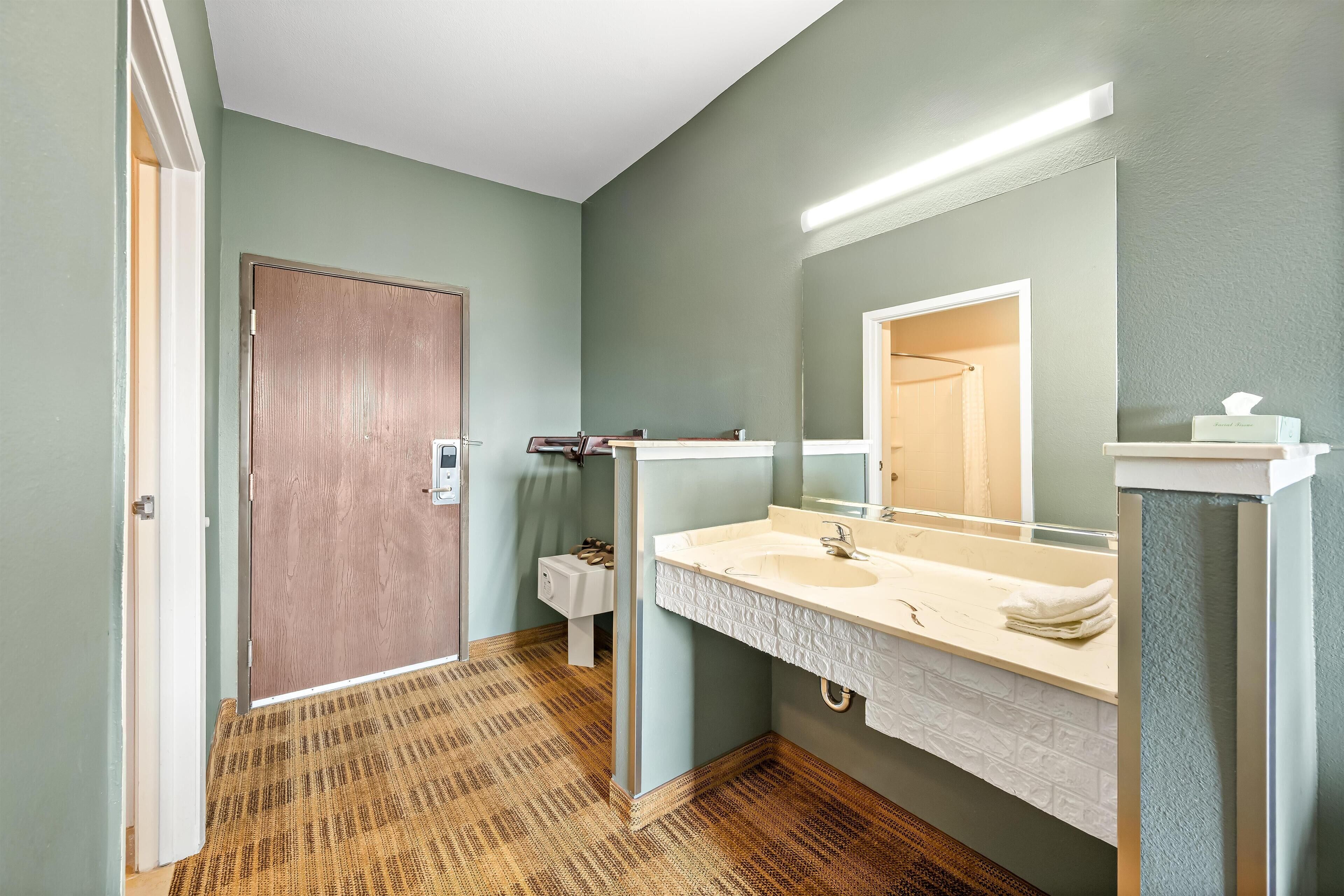 Un baño con puerta de madera, un lavamanos blanco con espejo y piso estampado.