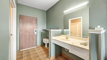 Un baño con puerta de madera, un lavamanos blanco con espejo y piso estampado.