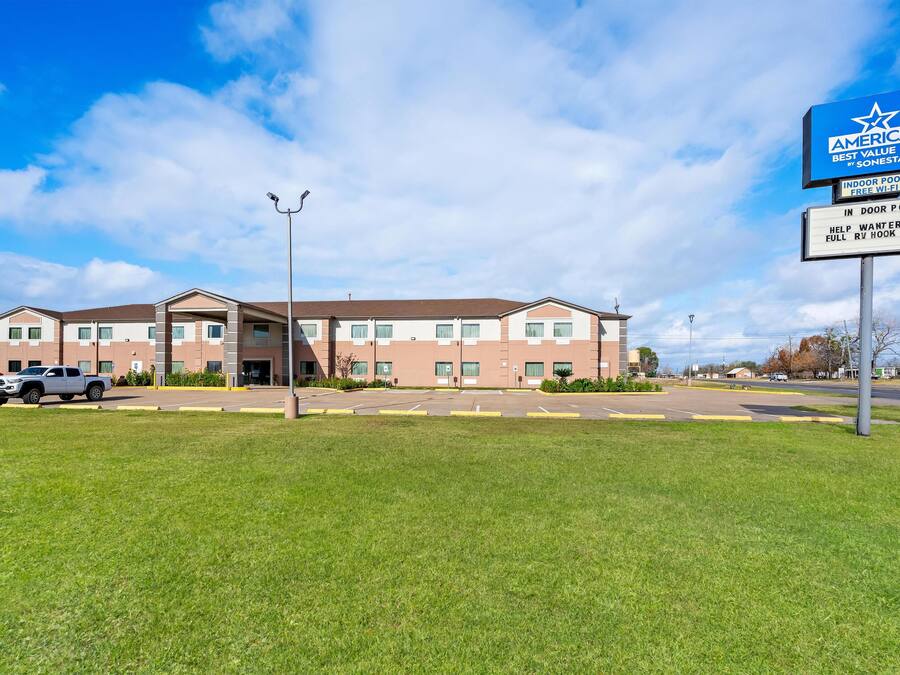 A hotel with a parking lot, a sign indicating an indoor pool and free WiFi, and a sign offering help for RV hook-ups.