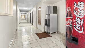 A hotel corridor with a Coca-Cola vending machine, a water cooler, and a brown mat on the floor. - Americas Best Value Inn Somerville (Somerville)