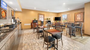 A hotel dining area with multiple tables and chairs, a counter with a coffee machine, and framed pictures on the walls. - Americas Best Value Inn Somerville (Somerville)