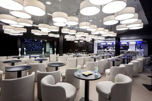 Uma área de estar moderna com diversas opções de assento, incluindo sofás e mesas redondas, e um espaço bar com balcão.