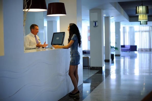 A reception area with a receptionist and a guest at the counter. - Playaolid Suites and Apartments (Adeje)