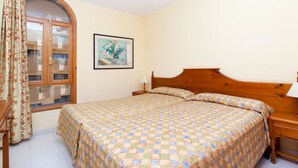 A bedroom with a wooden bed, a nightstand, a lamp, a window with curtains, and a framed picture on the wall. - Playaolid Suites and Apartments (Adeje)