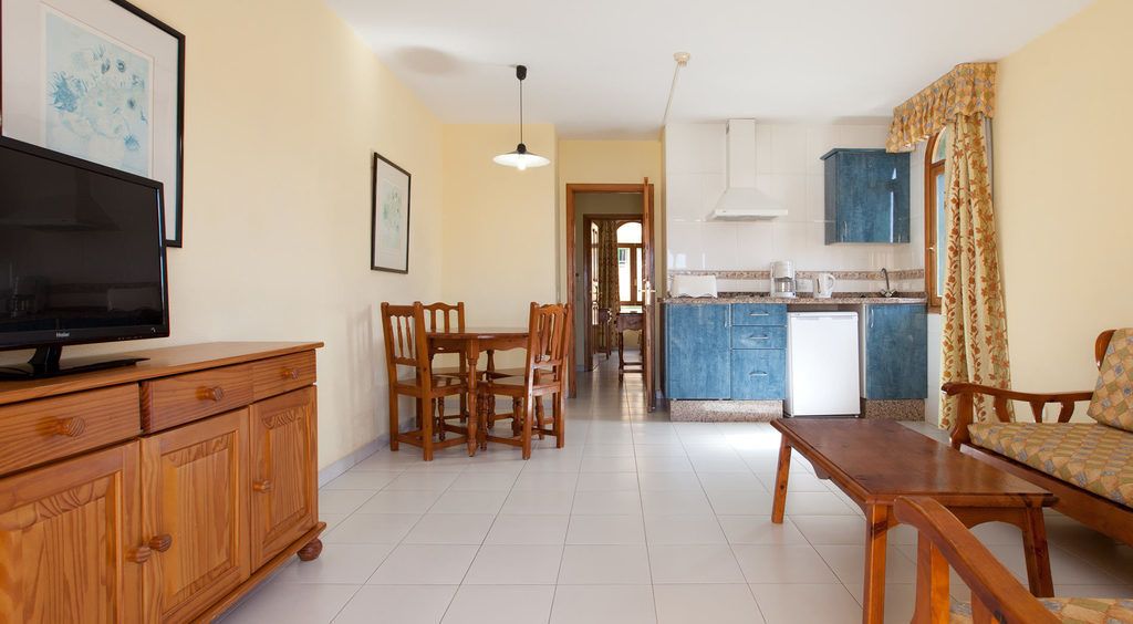 Una sala de estar con televisor, muebles de madera, un comedor y una cocina con armarios azules.
