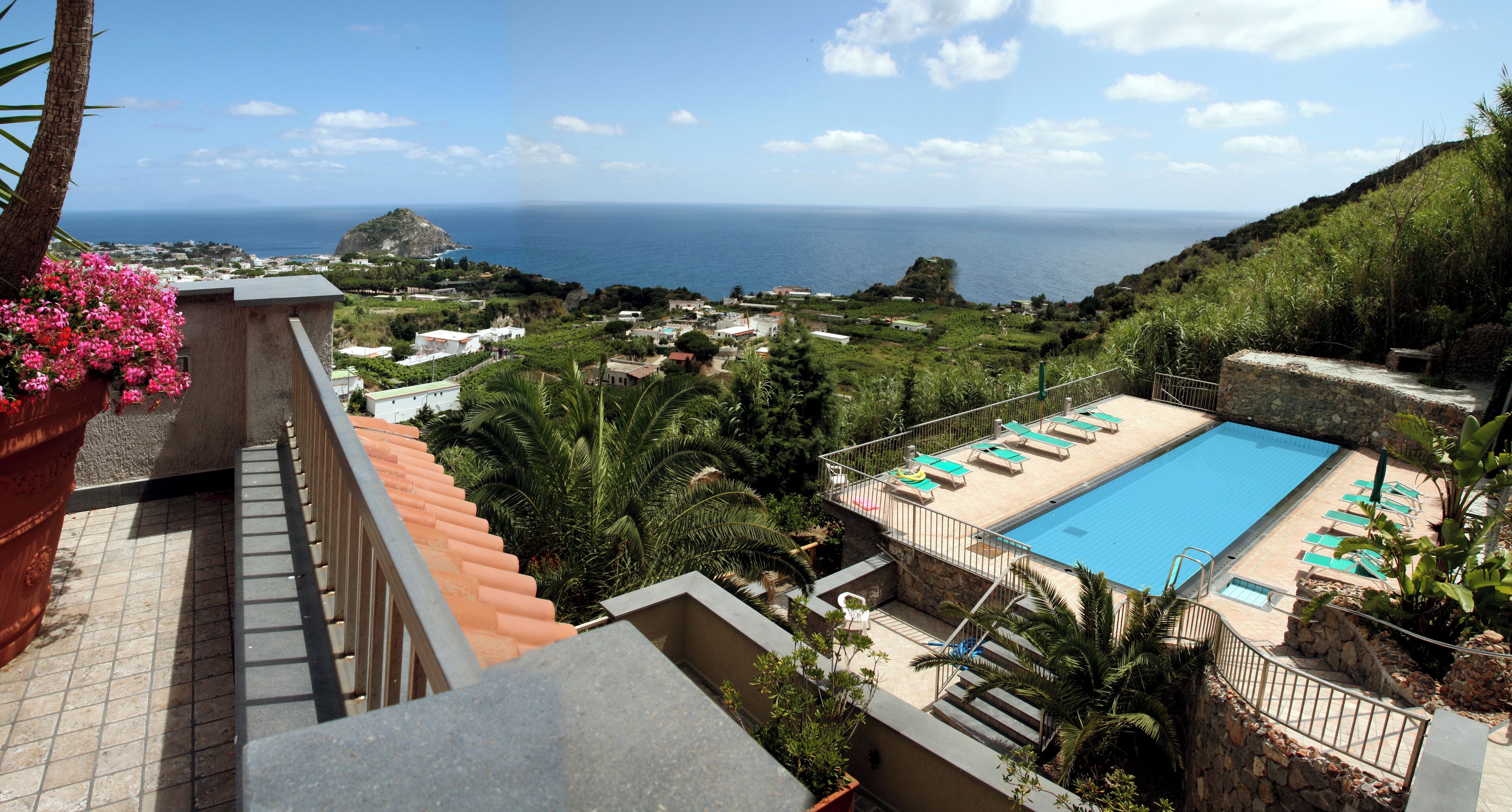 A pool area with lounge chairs and a view of the sea.