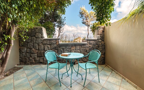 A patio with two turquoise chairs and a table, surrounded by stone walls and trees. - Punta Chiarito Resort (Forio)