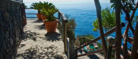 A stone staircase leading to a terrace overlooking the sea, with potted plants and a view of the ocean.