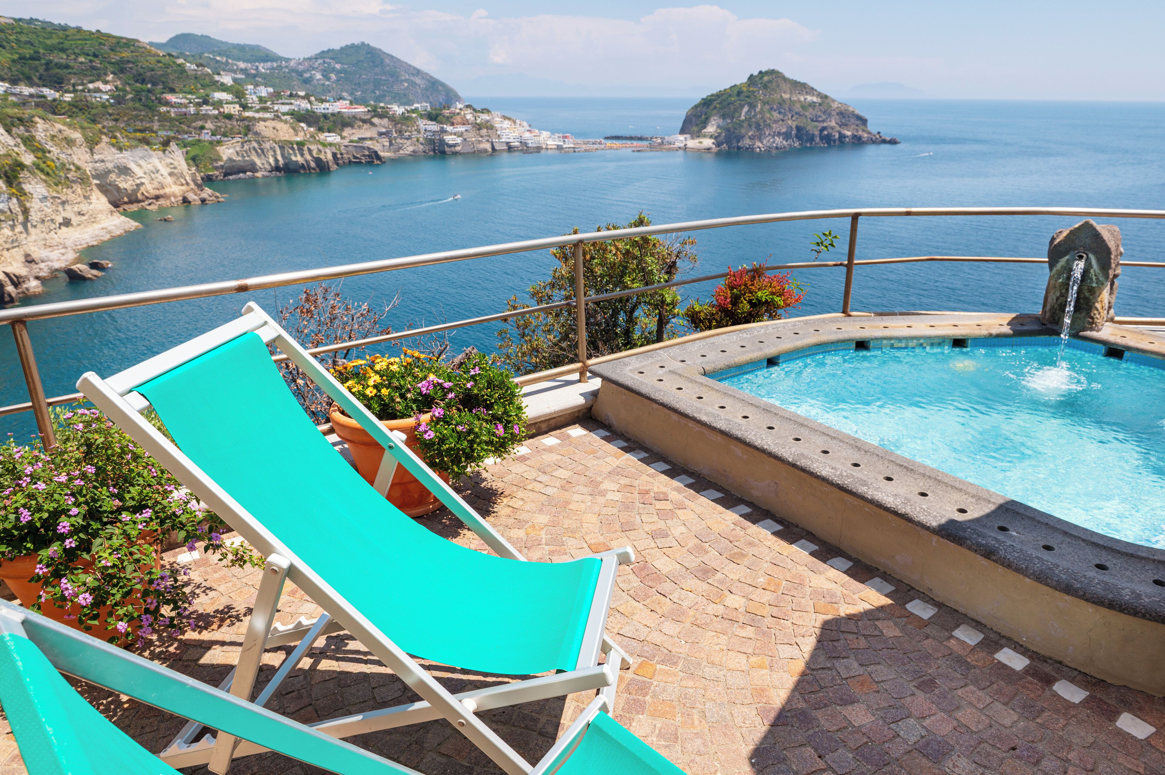 A pool area with a view of the sea, a small waterfall feature, and a couple of lounge chairs.
