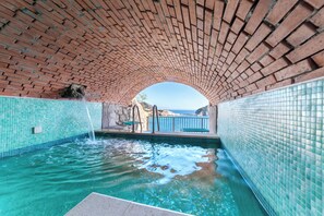 An indoor swimming pool with clear blue water, surrounded by tiled walls and a brick ceiling.