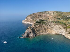 A coastal cliff with a clear view of the sea, a boat, and a small settlement with buildings.