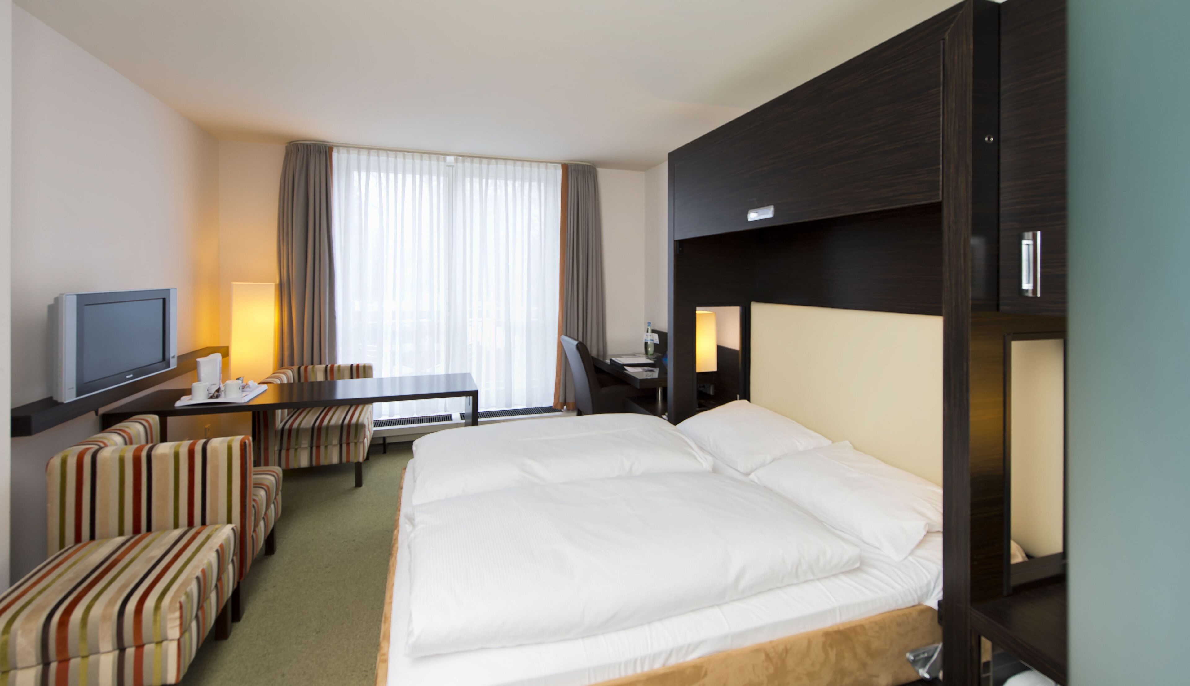 Una habitación de hotel con una cama grande, televisión, escritorio con silla y sofá.