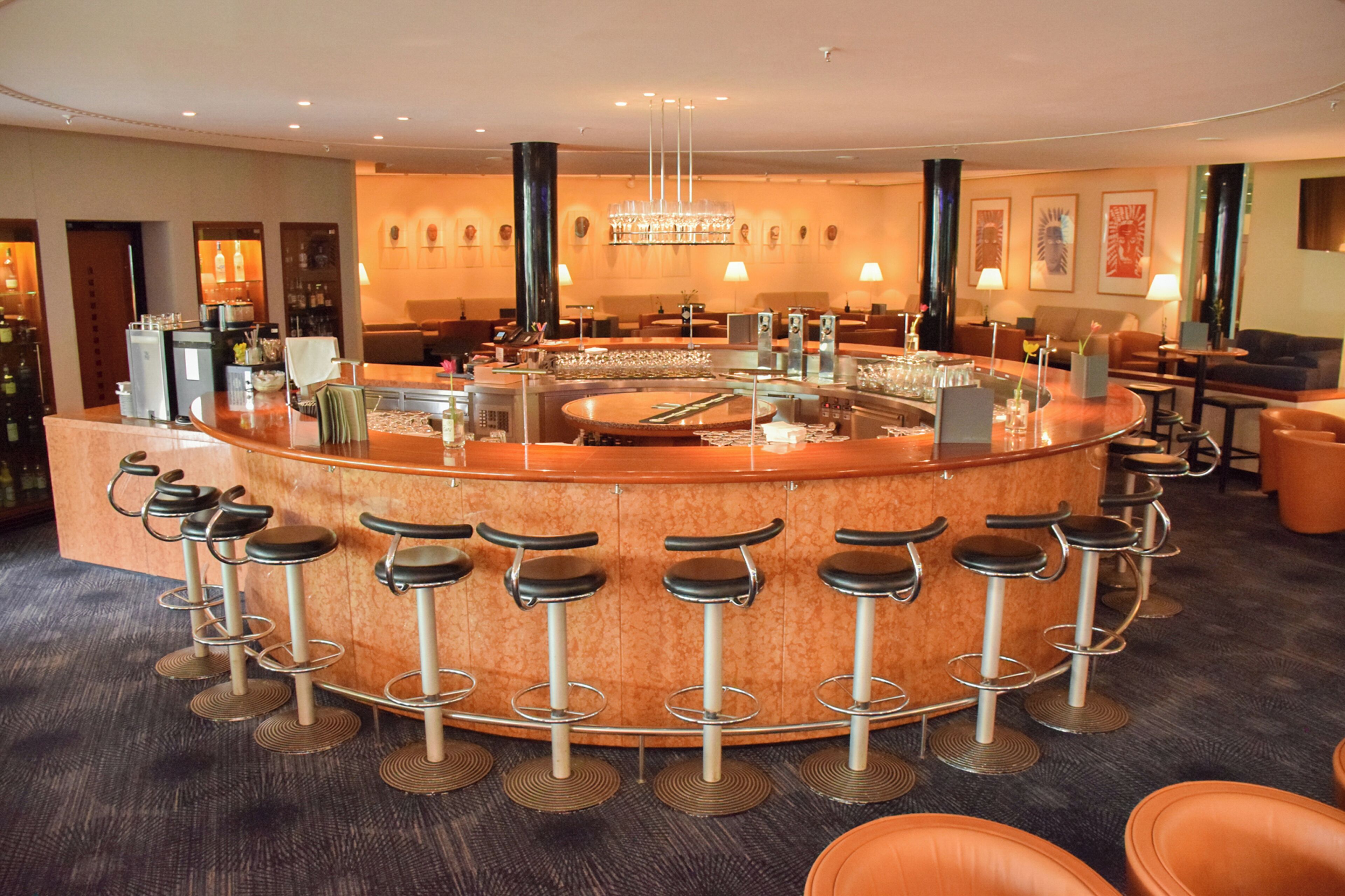 A bar area with a central bar, multiple stools, and a chandelier.