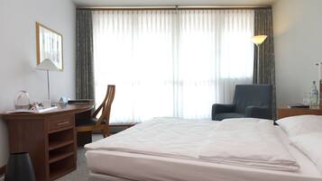 Habitación de hotel con cama, escritorio, silla, lámpara y ventana con cortinas.