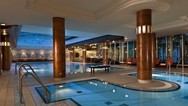 An indoor swimming pool with a tiled floor, metal railings, and large columns. - City Hotel Dresden Radebeul (Radebeul)