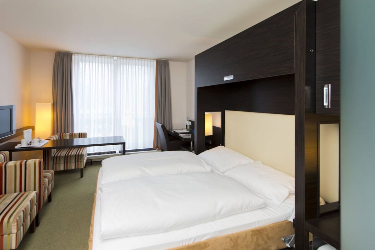 A hotel room with a large bed, a desk with a chair, a television, and a sofa.