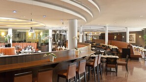 A modern restaurant with a curved counter, bar stools, and high ceilings with recessed lighting. - City Hotel Dresden Radebeul (Radebeul)
