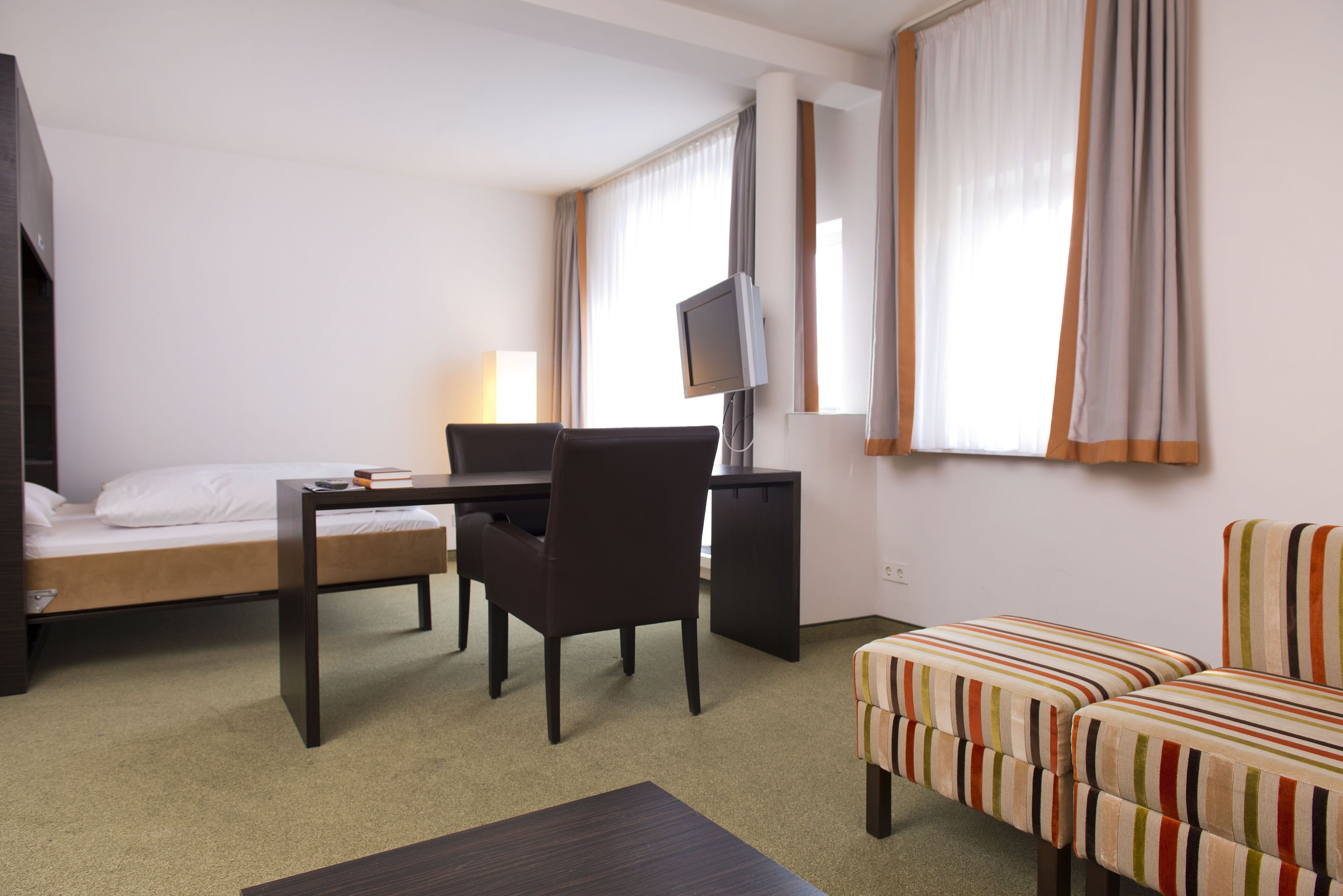 Une chambre d’hôtel avec un lit, un bureau et une chaise, une télévision et un canapé à rayures.
