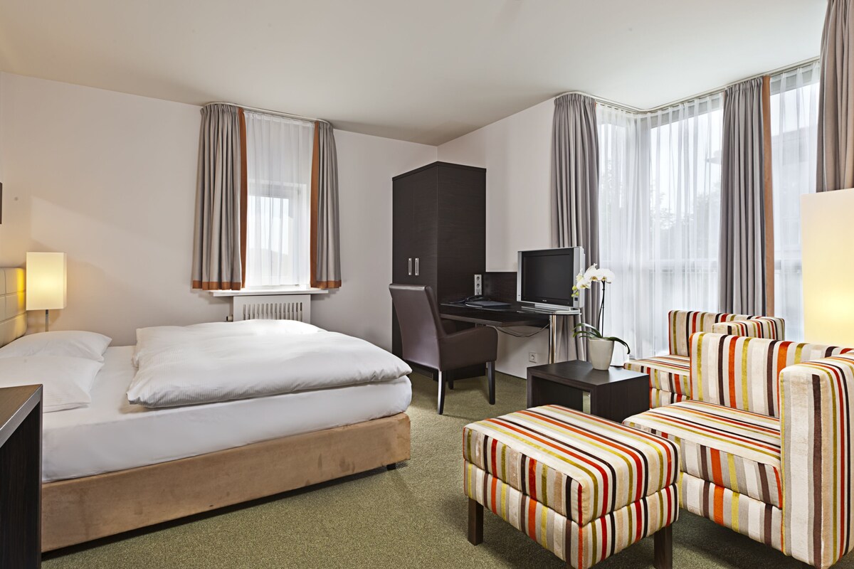 A hotel room with a bed, a desk with a computer, a chair, a sofa, and a TV.