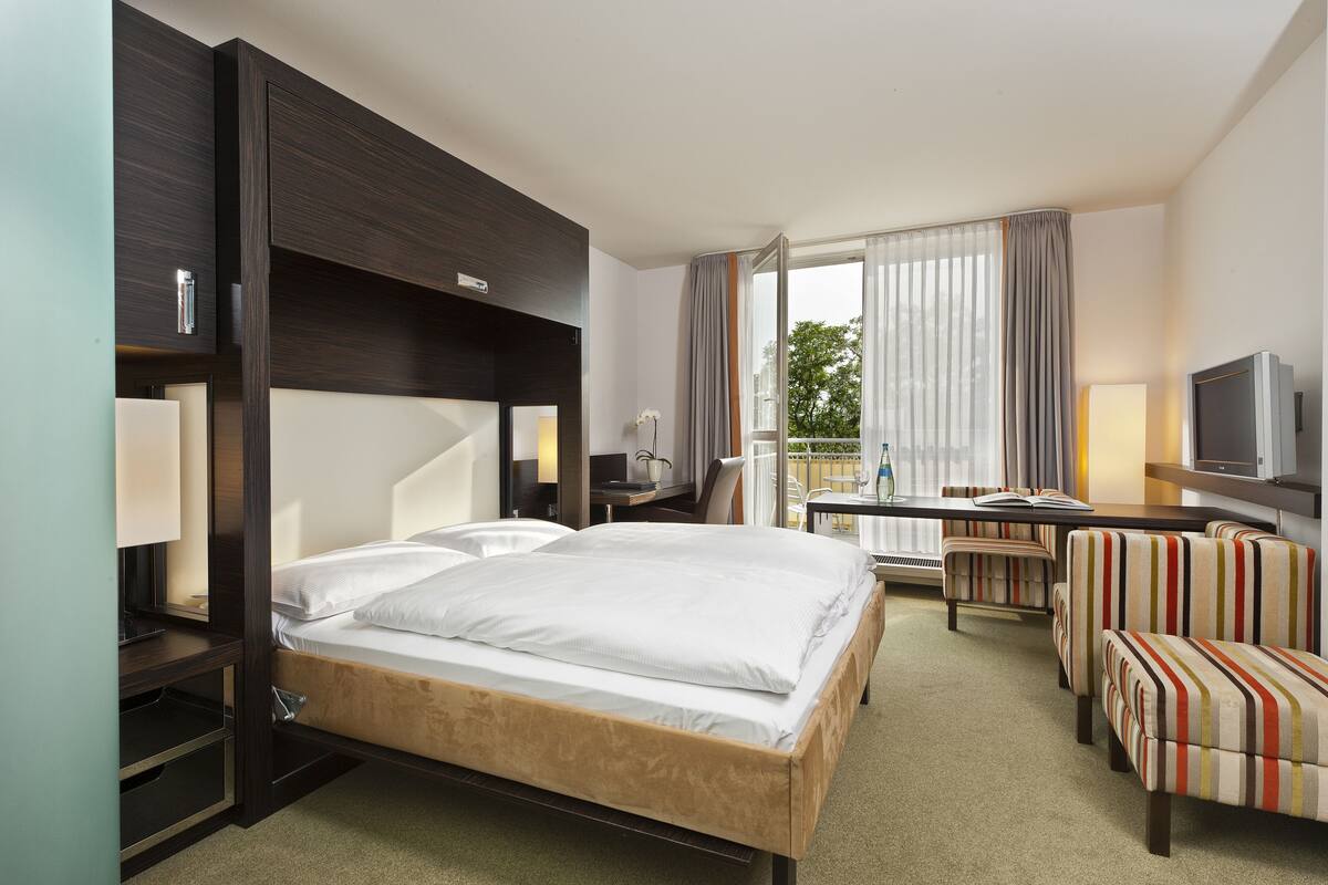 A hotel room with a bed, a desk, a TV, and a seating area.