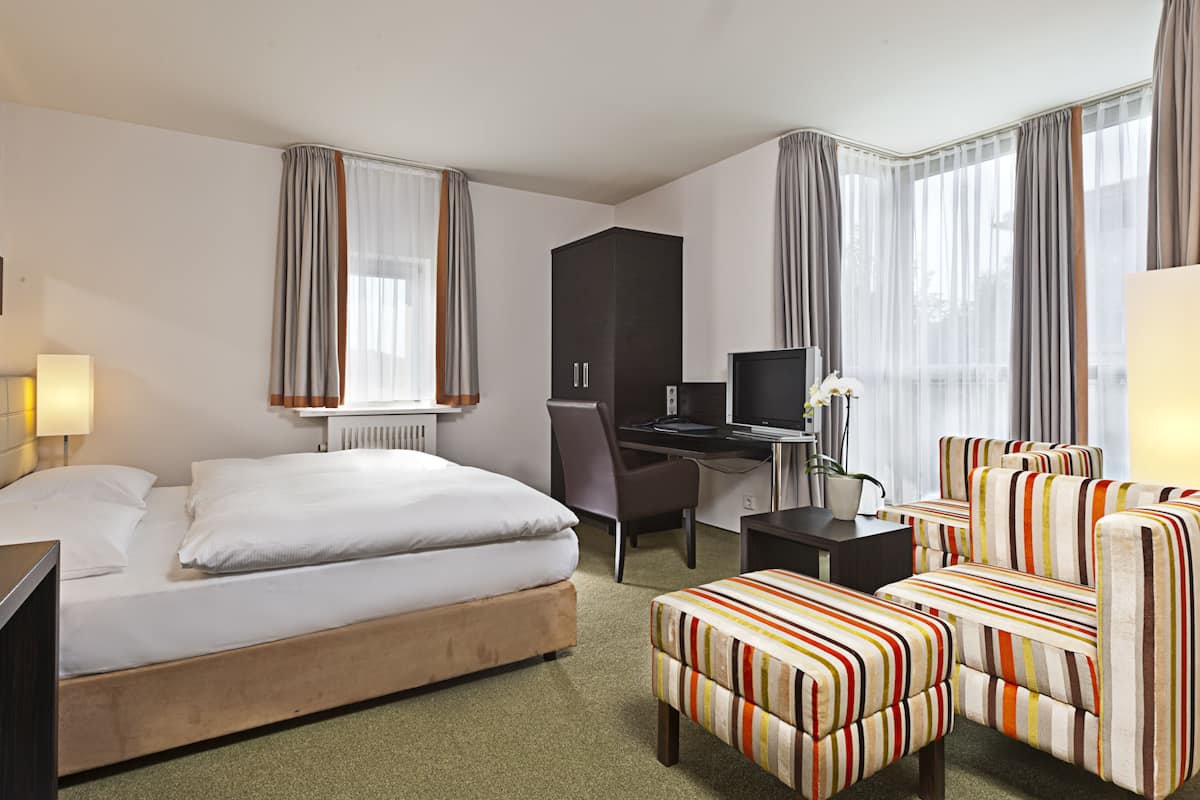 A hotel room with a bed, a desk with a computer, a chair, a sofa, and a TV.