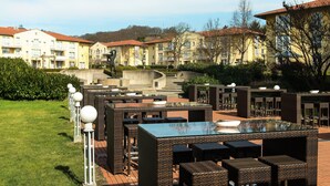 An outdoor patio area with wicker furniture, a glass-top table, and a pool. - City Hotel Dresden Radebeul (Radebeul)
