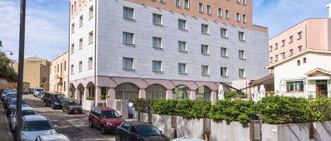 Un hotel de varios pisos con fachada moderna, un estacionamiento con varios autos y un cielo despejado.