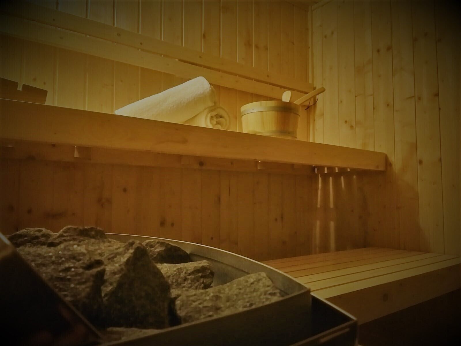 Una sauna con pareti in legno, una panca, una vasca in pietra e un contenitore di legno.