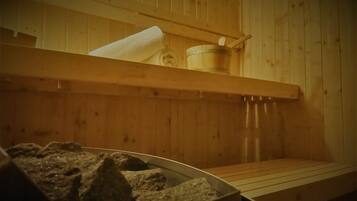 Una sauna con pareti in legno, una panca, una vasca in pietra e un contenitore di legno.