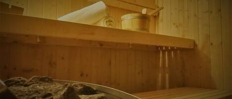 Un cuarto de sauna con paredes de madera, un banco, una pileta de piedra y un recipiente de madera.