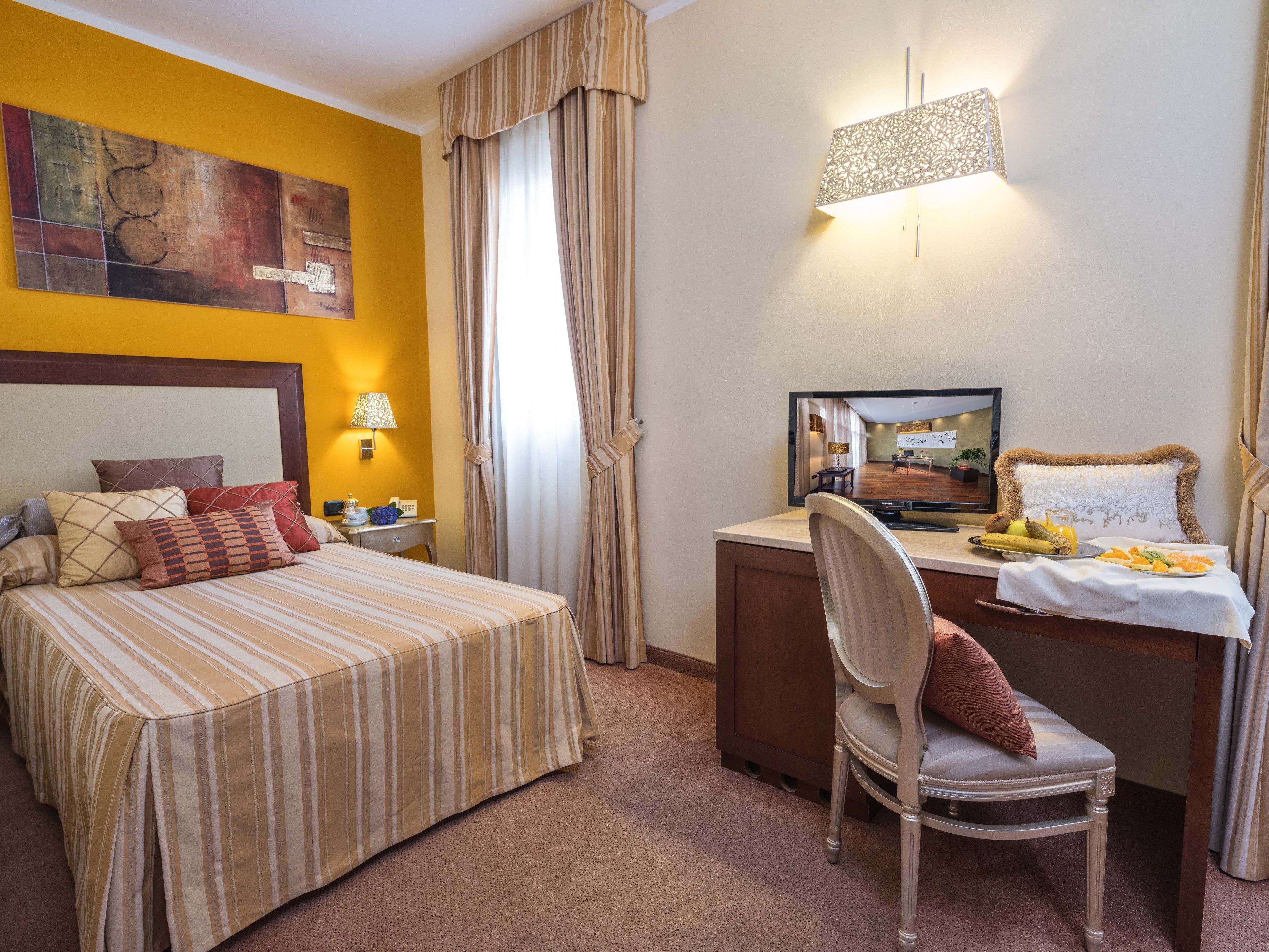 Quarto de hotel com cama, escrivaninha, cadeira, televisão e área de refeições com frutas.