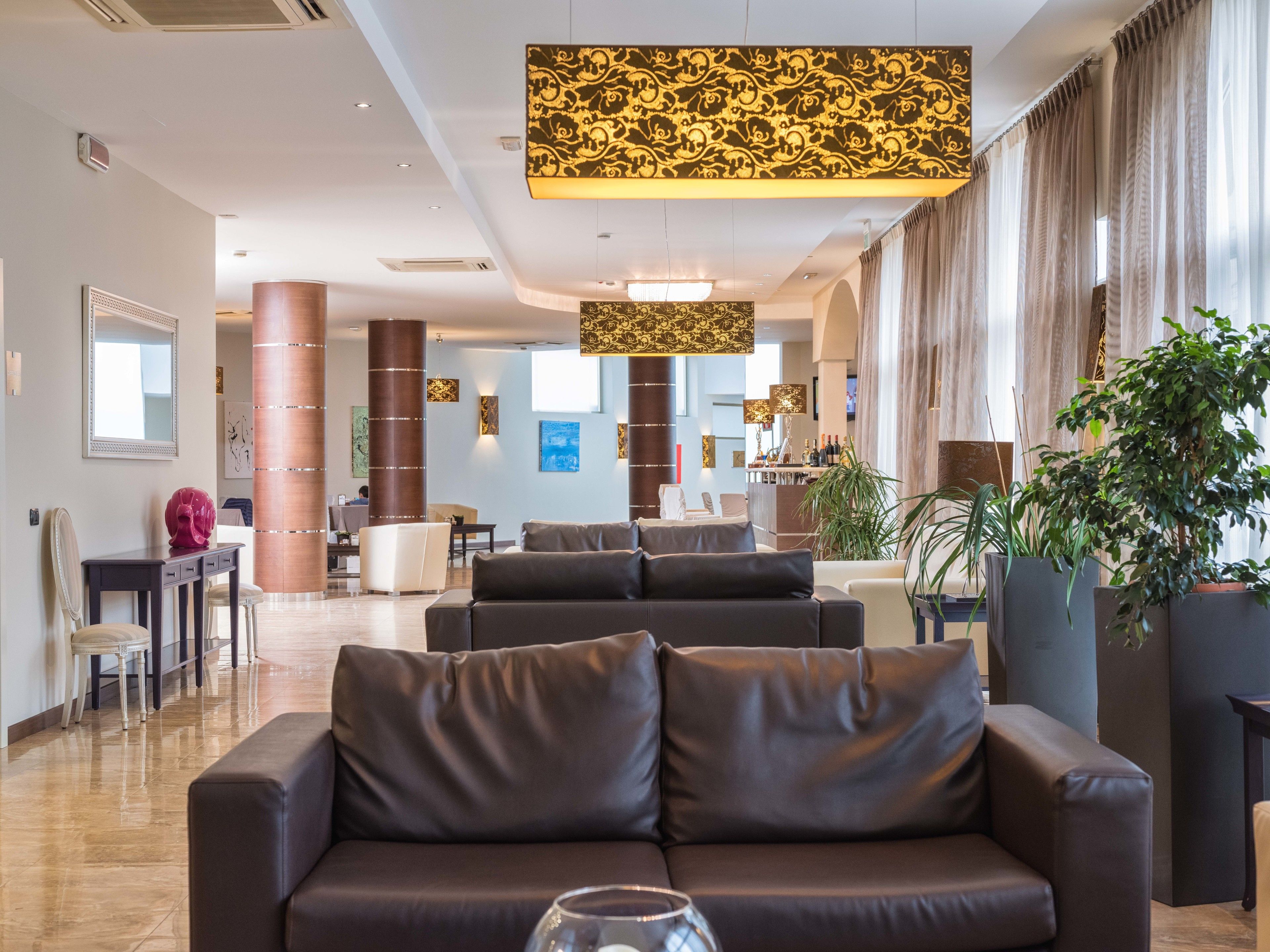 A spacious lobby with a modern design, featuring a leather sofa, a reception desk, and a bar area.