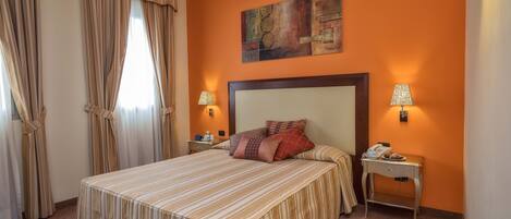 A hotel room with a large bed, two bedside tables, a nightstand, a painting on the wall, and a window with curtains.