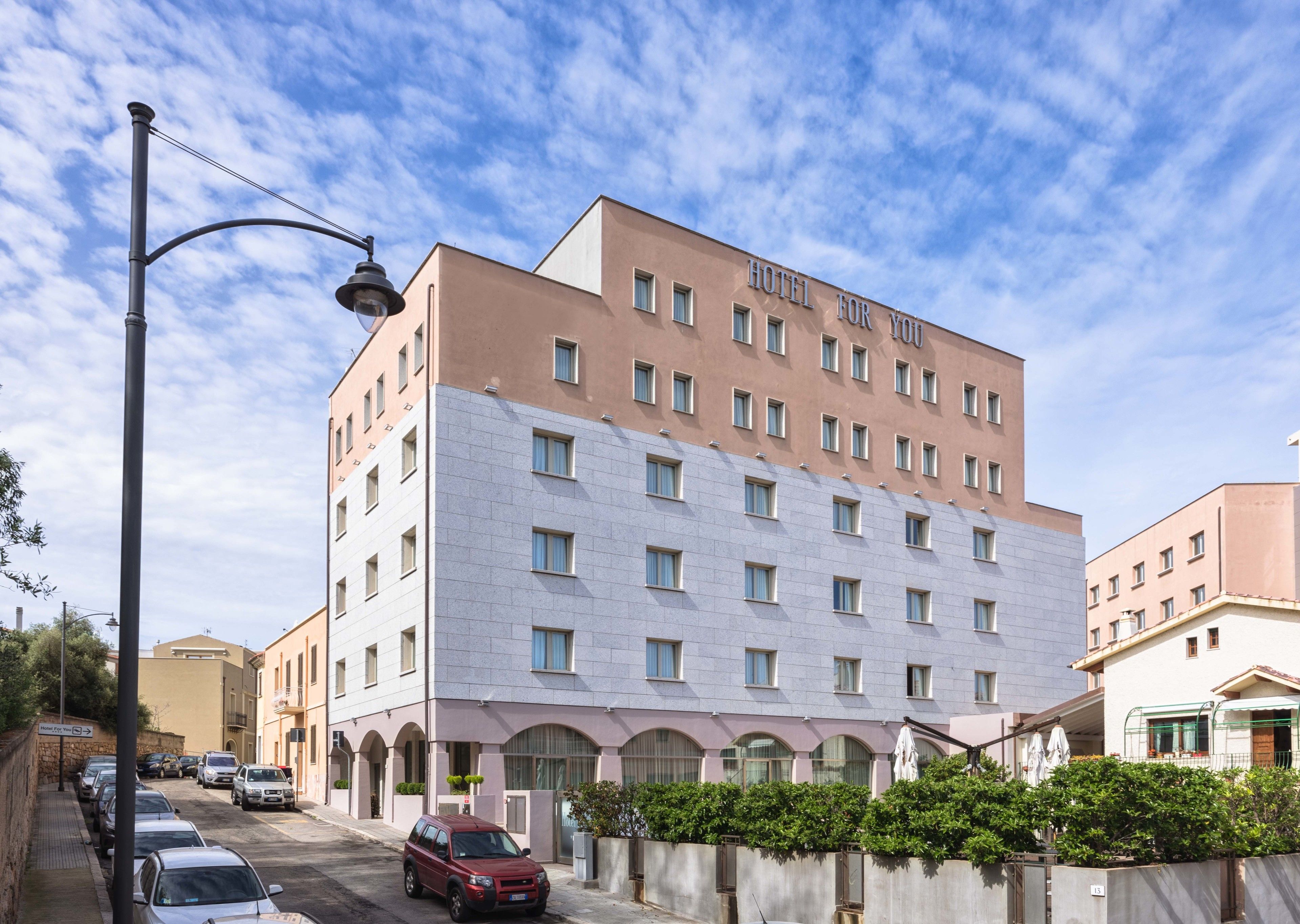 Un hotel de varios pisos con fachada moderna, que combina piedra y enlucido en su exterior, y un cielo azul despejado al fondo.