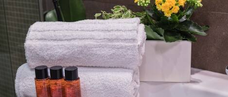 A bathroom with a white sink, rolled white towels, and three bottles of shampoo.