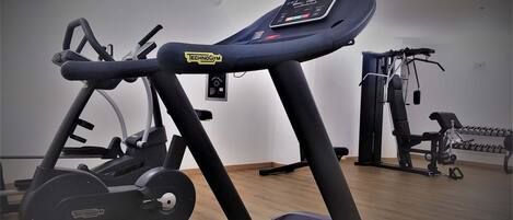 Una cinta de correr con pantalla digital y una banca de pesas al fondo.