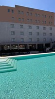 A hotel with a swimming pool, multiple balconies, and a clear blue sky.